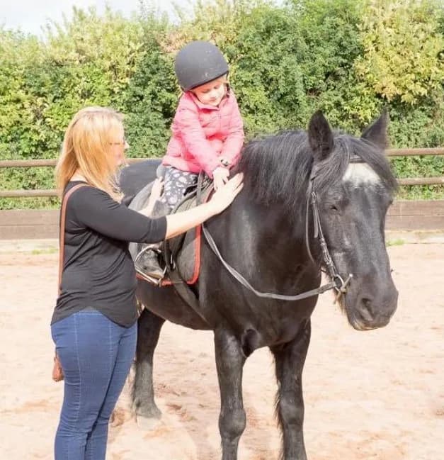 Young child riding a pony with an instructor at Woodside Riding School, Bestwood