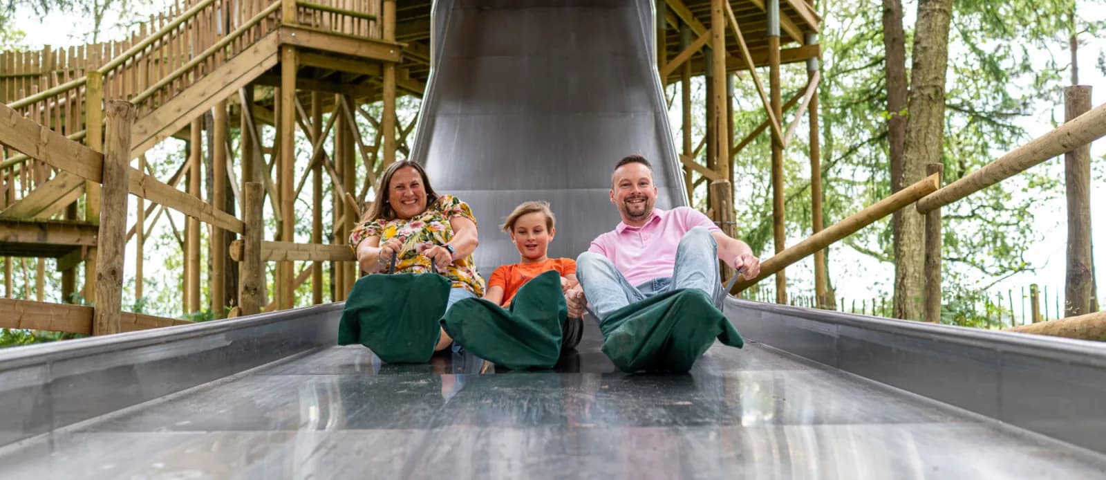 Family riding the wide Slippery Slopes slide on mats at BeWILDerwood Norfolk