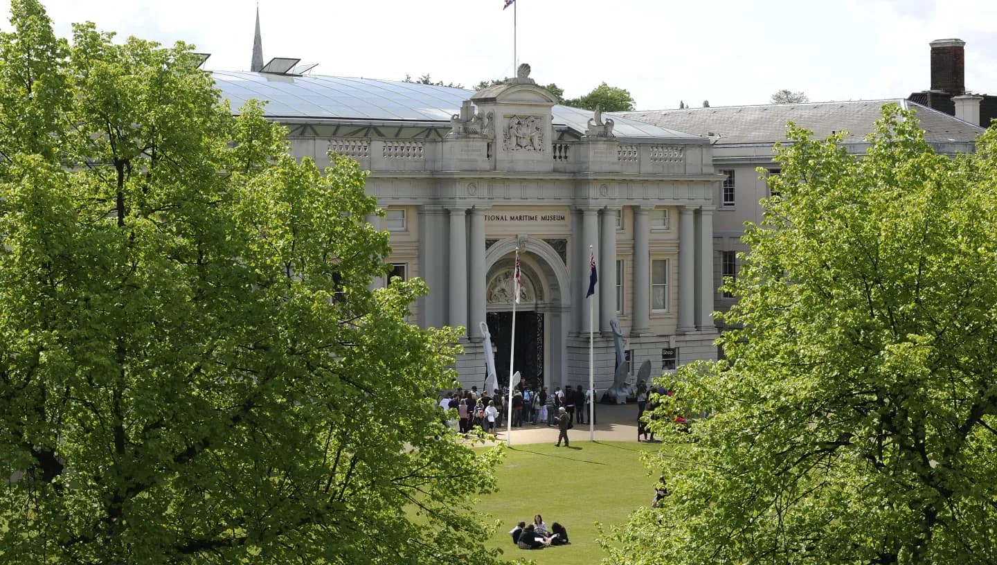 The exterior of the National Maritime Museum in Greenwich, a grand neoclassical building with flags and visitors at the entrance