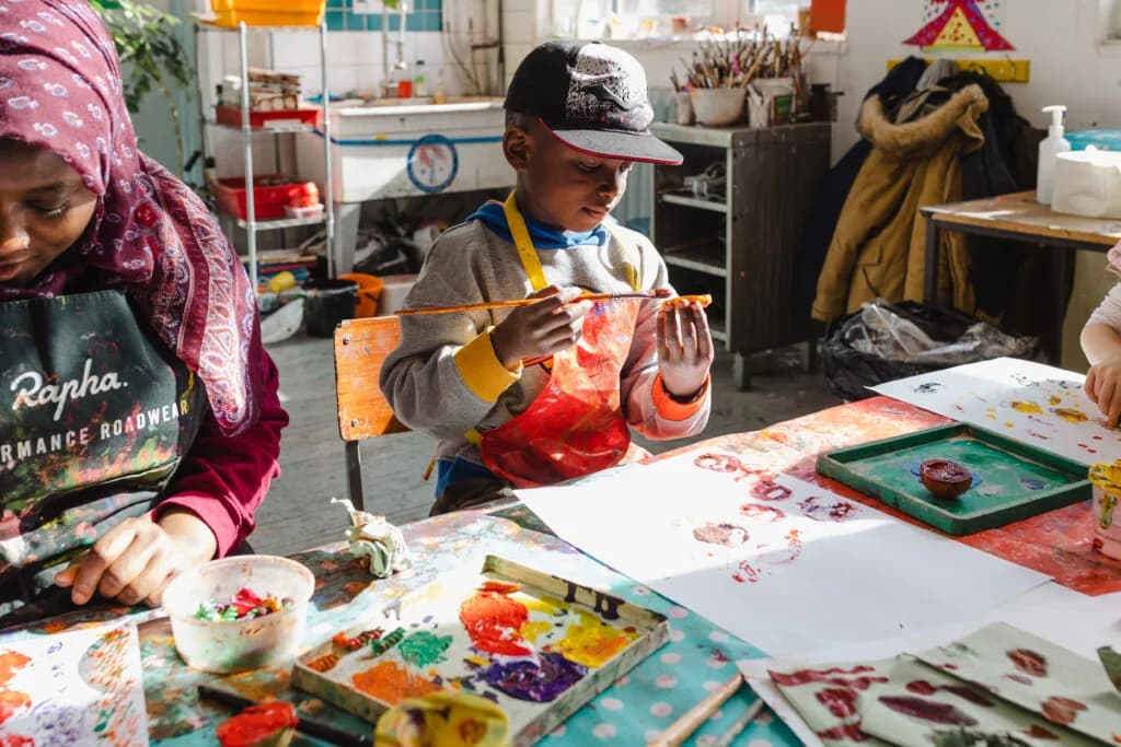 Children and an adult joyfully create colourful art with paint and stamps in a bright studio