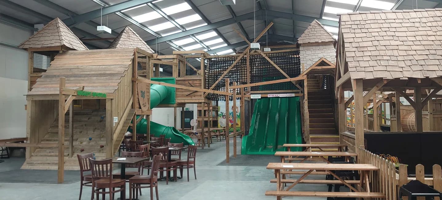 Bright indoor adventure play barn at Wiggleys Fun Farm with multi-level wooden play structures, green slides and climbing nets