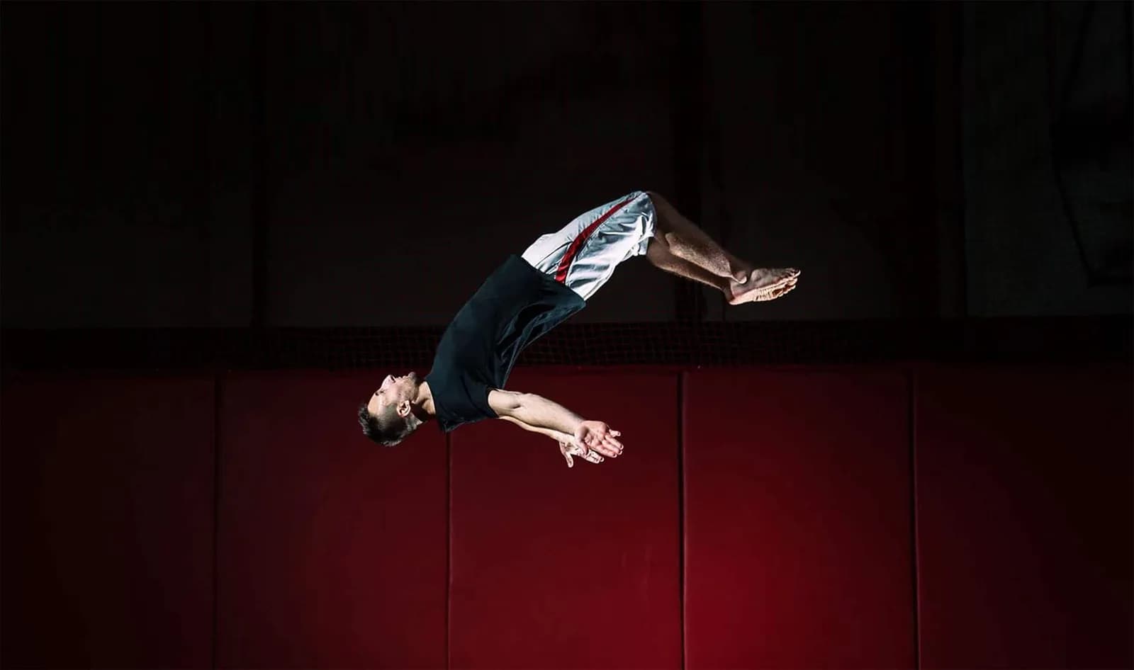 Jumper performing an acrobatic flip in mid-air over red padded walls at Infinity Trampoline Park Cardiff