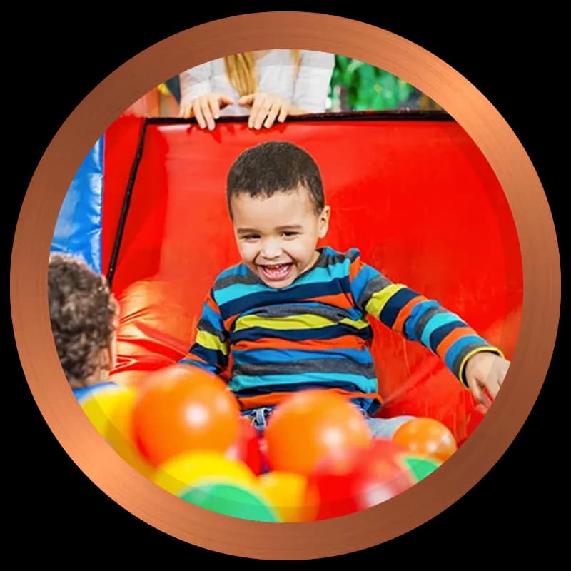 Child laughing in a colourful ball pit on red soft play equipment at Jam Jam Boomerang