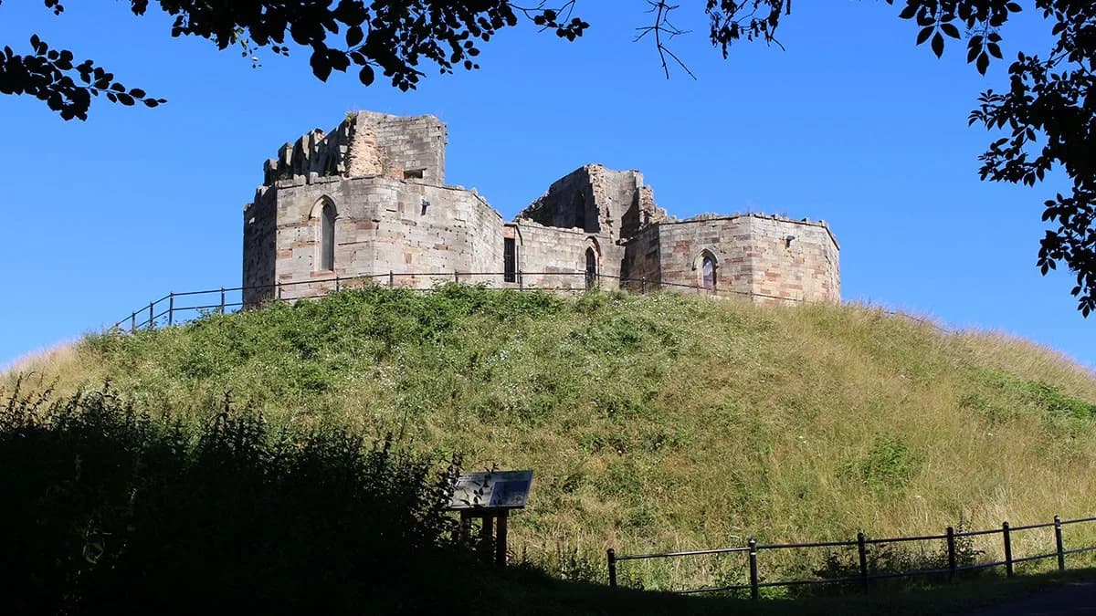 Stafford Castle keep ruins on the motte, seen through trees on a sunny day