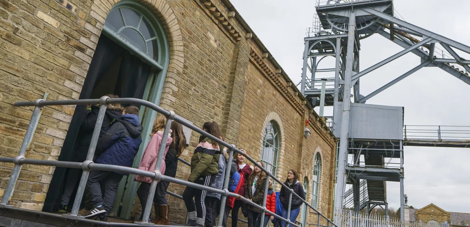 Visitors walking into the historic colliery building beside the headframe at Woodhorn Museum