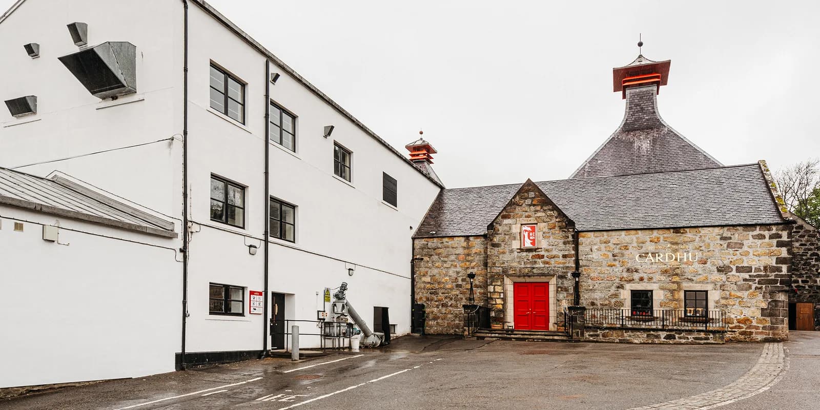The brown stone building of the Cardhu distillery with a pitched slate roof and red door