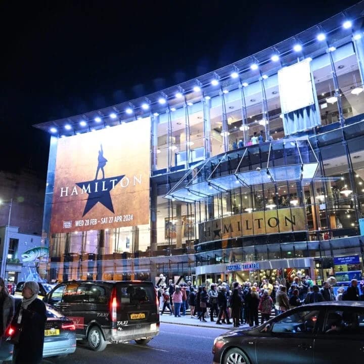 Festival Theatre Edinburgh at night, with a large Hamilton musical banner and theatre-goers on the street below
