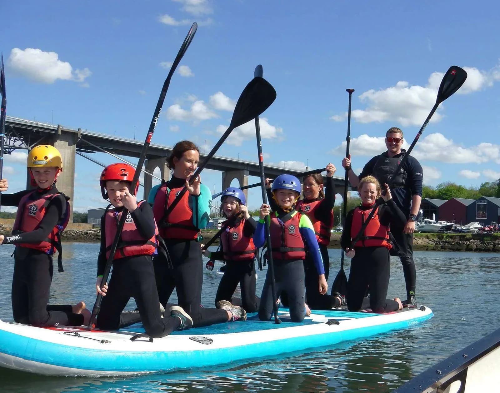 Children and an instructor paddle a giant stand-up paddleboard at Edinburgh Watersports, Port Edgar Marina