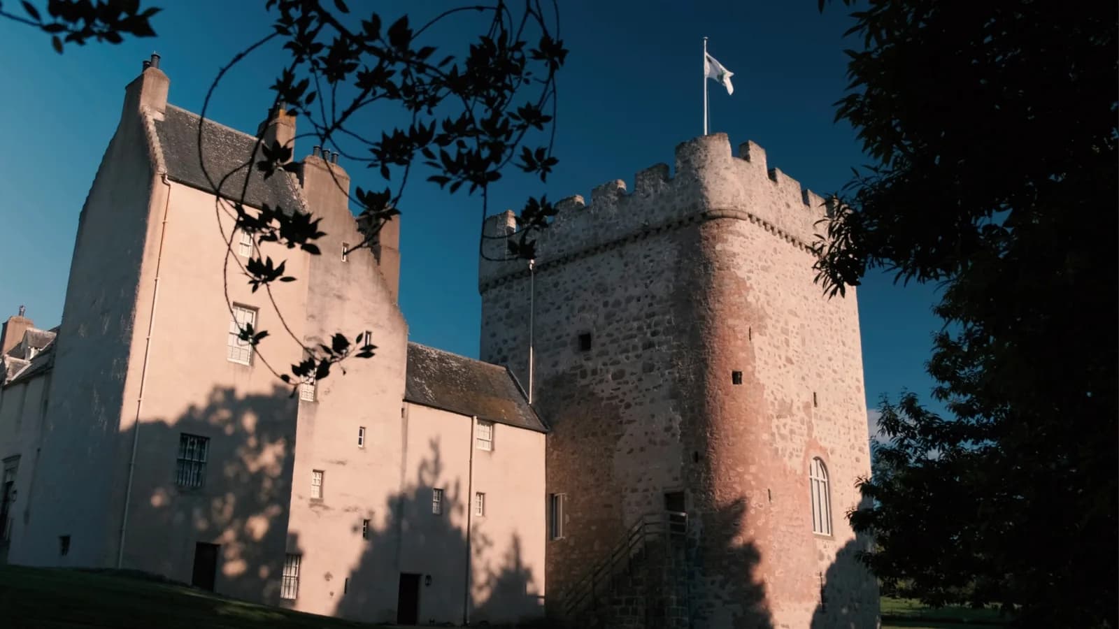 Drum Castle tower house with flag, viewed through trees