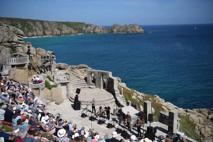 Minack Theatre's open-air clifftop amphitheatre with tiered stone seating and sea views during a live performance