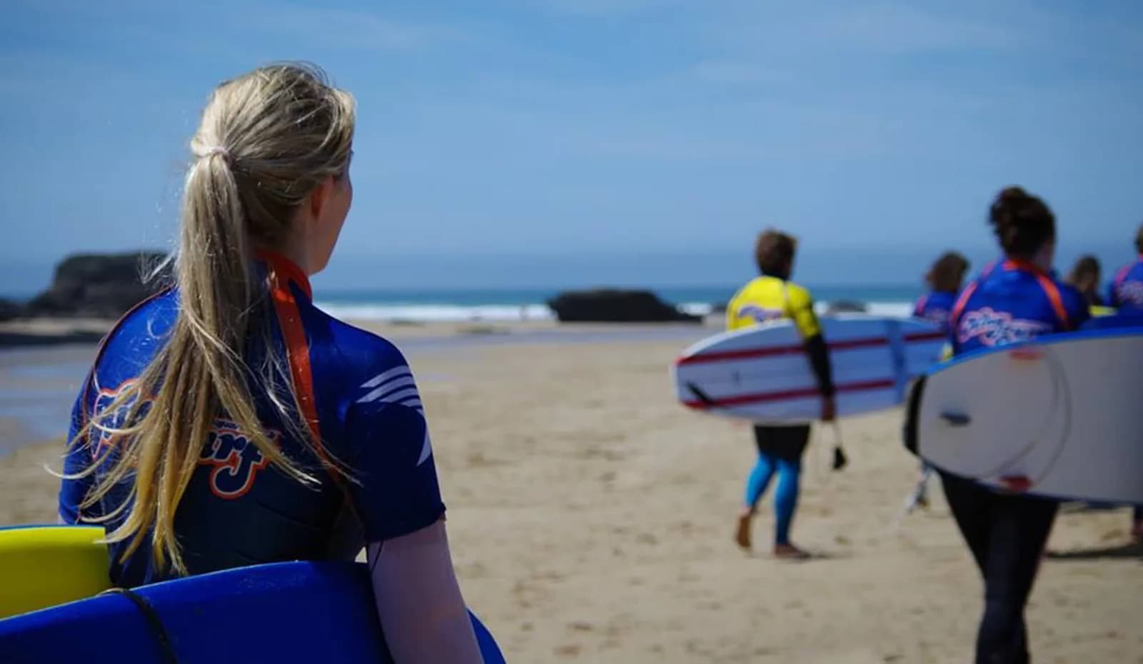 Surf lesson group carrying boards into the sea at Mawgan Porth beach, Kingsurf Surf School
