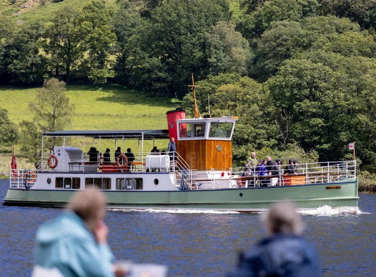 An Ullswater Steamer cruises past walkers on the shore of Ullswater Lake