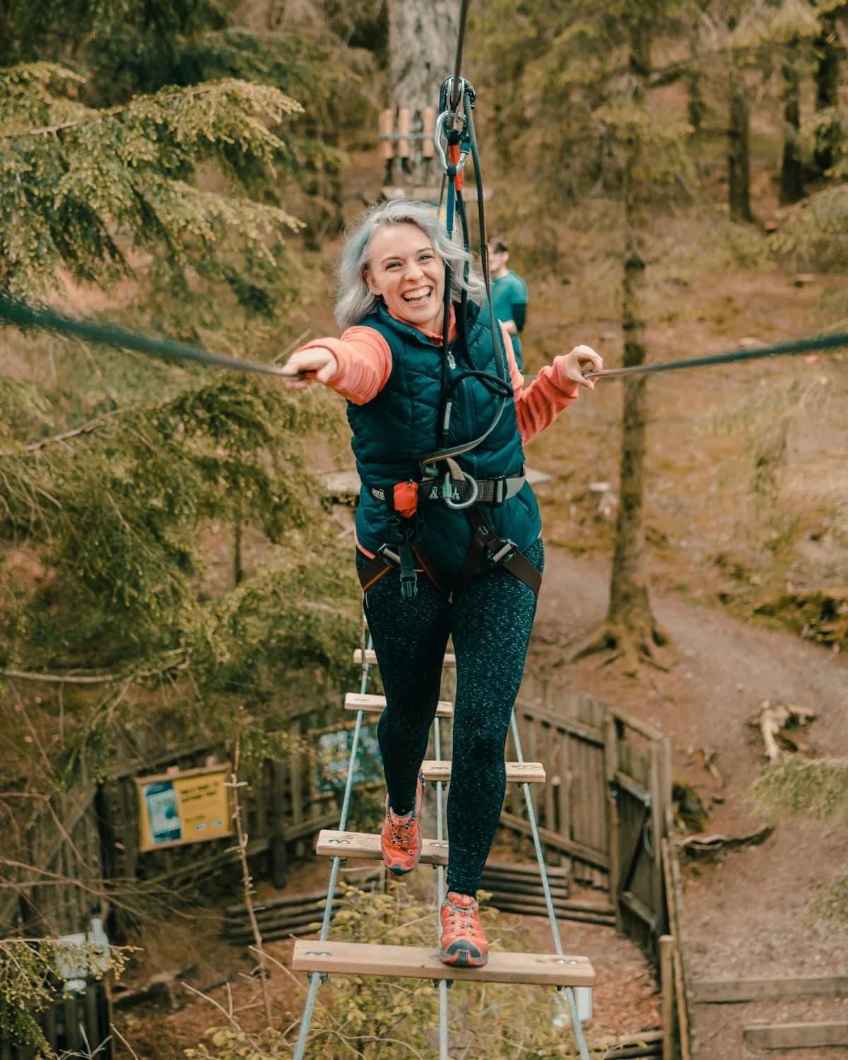 Woman laughing as she balances on a rope ladder high in the trees at Go Ape Whinlatter forest adventure course
