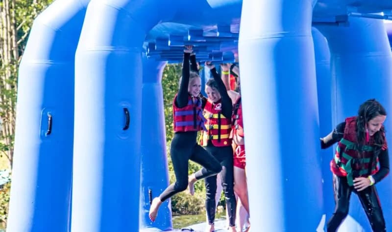 Children in wetsuits and life vests climb across the inflatable water obstacle course at Alderford Lake
